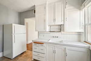 Kitchen with freestanding refrigerator, a sink, tile countertops, and white cabinetry