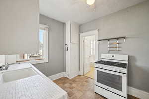 Kitchen featuring gas range gas stove, a sink, ceiling fan, baseboards, and white cabinetry