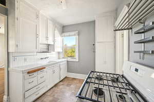 Kitchen with tile counters, open shelves, baseboards, gas range gas stove, and white cabinetry