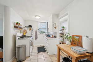 Kitchen with white gas range, white cabinetry, light tile patterned flooring, light countertops, and a sink