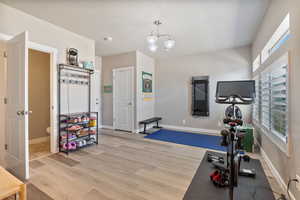 Workout area with light wood-style floors, a chandelier, and baseboards
