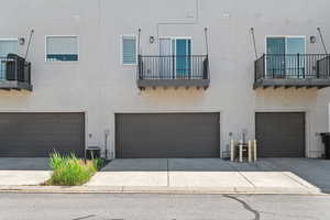 View of front of house featuring an attached garage, stucco siding, driveway, and a balcony