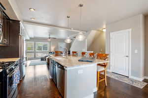 Kitchen with a breakfast bar, appliances with stainless steel finishes, a sink, dark wood-style flooring, and dark brown cabinetry
