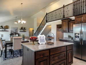 Kitchen with stainless steel refrigerator with ice dispenser, light tile patterned floors, a ceiling fan, dark brown cabinetry, and a center island