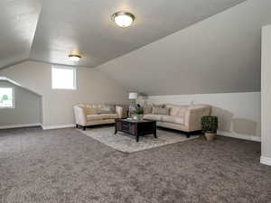 Carpeted living room with a textured ceiling, vaulted ceiling, and baseboards