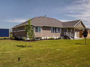 Back of house with a lawn, a shingled roof, and stucco siding