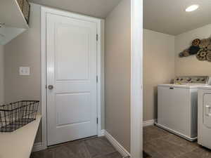 Laundry room with washer and dryer, dark tile patterned floors, and baseboards