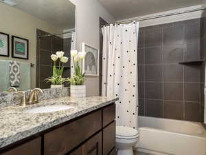 Full bathroom with toilet, a textured ceiling, vanity, and shower / bath combo