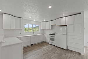 Kitchen featuring white appliances, a sink, recessed lighting, a textured ceiling, and light wood-type flooring