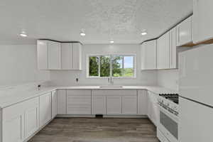 Kitchen with white appliances, a sink, recessed lighting, a textured ceiling, and white cabinetry