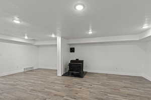 Finished below grade area with a wood stove, a textured ceiling, wood finished floors, and baseboards