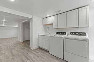 Clothes washing area with a sink, washer and clothes dryer, light wood-style flooring, a textured ceiling, and baseboards