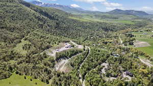 Aerial view of property and surrounding area featuring a mountain backdrop and a forest