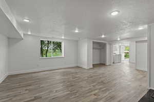 Unfurnished living room featuring washing machine and clothes dryer, light wood-type flooring, a textured ceiling, baseboards, and recessed lighting