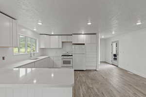 Kitchen featuring white appliances, a sink, a peninsula, light stone counters, and light wood-style flooring
