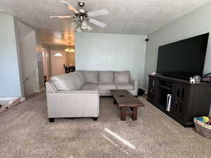 Carpeted living room featuring a textured ceiling, ceiling fan, and a chandelier