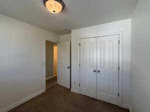 Unfurnished bedroom featuring dark carpet, a closet, and a textured ceiling