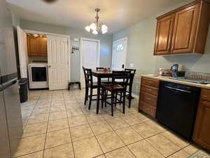 Kitchen featuring brown cabinetry, washer / clothes dryer, black dishwasher, light countertops, and decorative light fixtures