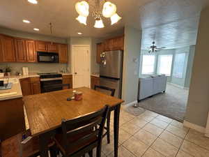 Kitchen featuring light countertops, black appliances, a textured ceiling, light tile patterned floors, and brown cabinetry