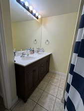 Full bathroom with a textured ceiling, light tile patterned flooring, double vanity, and a textured wall