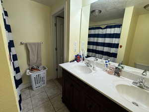 Full bathroom featuring double vanity, light tile patterned floors, a shower with curtain, a textured ceiling, and a textured wall