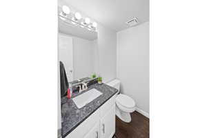 Bathroom with toilet, wood finished floors, vanity, baseboards, and a textured ceiling