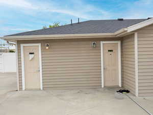 Property entrance with roof with shingles, fence, and a patio area