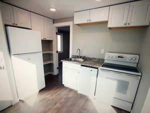 Unit B Kitchen with white appliances, a sink, light wood-style flooring, and white cabinetry