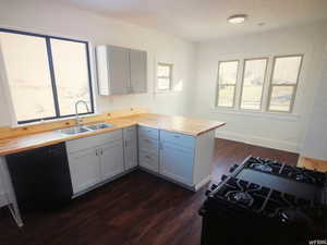 Kitchen with butcher block counters, a sink, a peninsula, dark wood-type flooring, and black appliances