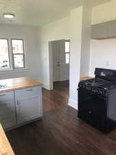 Kitchen with black range with gas cooktop, butcher block counters, dark wood-style floors, baseboards, and gray cabinetry