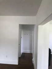 Hall with baseboards, wood finished floors, and a textured ceiling