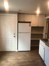 Unit B Kitchen featuring white appliances, white cabinets, dark countertops, and dark wood-style floors