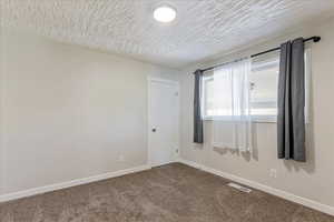 Empty room with dark colored carpet, baseboards, and a textured ceiling