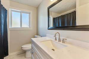 Full bath with a textured ceiling, toilet, marble look tiles, vanity, and baseboards