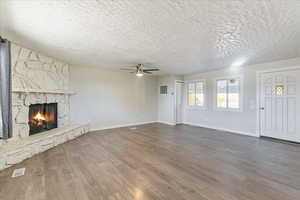 Unfurnished living room featuring ceiling fan, a textured ceiling, a fireplace, baseboards, and wood finished floors