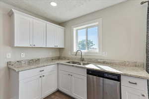 Kitchen with stainless steel dishwasher, a sink, white cabinets, light stone countertops, and recessed lighting