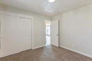 Unfurnished bedroom with carpet flooring, a closet, baseboards, and a textured ceiling