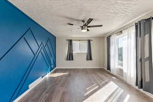 Empty room with healthy amount of natural light, wood finished floors, ceiling fan, a textured ceiling, and baseboards