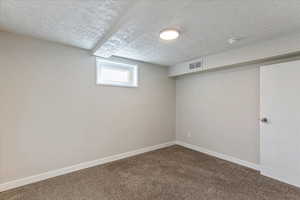 Below grade area featuring a textured ceiling, dark colored carpet, and baseboards