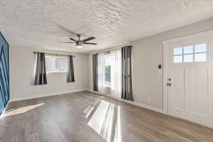 Entrance foyer featuring healthy amount of natural light, ceiling fan, baseboards, wood finished floors, and a textured ceiling
