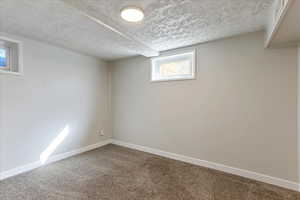 Basement featuring dark colored carpet, baseboards, and a textured ceiling