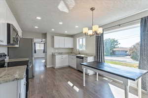 Kitchen with stainless steel appliances, a chandelier, a textured ceiling, white cabinetry, and recessed lighting