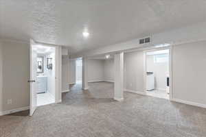 Below grade area with a textured ceiling, light carpet, washer / clothes dryer, and baseboards