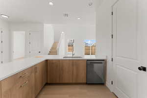 Kitchen featuring stainless steel dishwasher, a sink, light countertops, light wood-style flooring, and recessed lighting