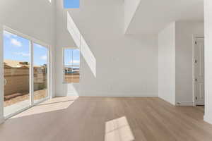 Unfurnished living room with light wood finished floors, a high ceiling, and baseboards