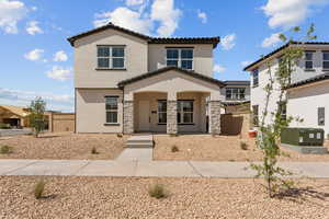 View of front facade featuring a tiled roof, stucco siding, stone siding, and covered porch