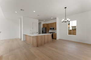 Kitchen featuring appliances with stainless steel finishes, brown cabinetry, light wood-style floors, a chandelier, and light countertops