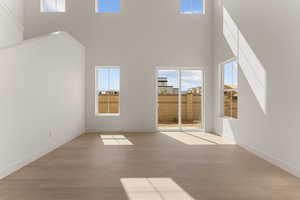 Unfurnished living room with a high ceiling, light wood-style flooring, and baseboards
