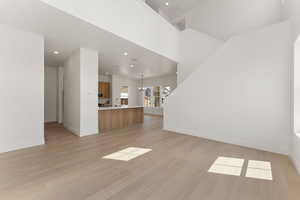 Unfurnished living room with baseboards, light wood-type flooring, recessed lighting, a sink, and a chandelier