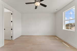 Spare room featuring light wood-style floors, ceiling fan, and baseboards